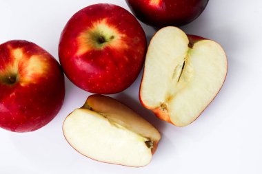 Several whole red apples are placed next to freshly cut halves, revealing the core, on a clean white background.