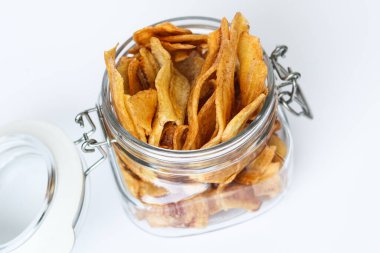 A glass jar filled with crispy banana chips. Captured with natural light on a white background.