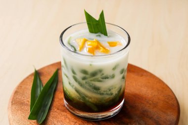 One glass of cold cendol, an Indonesian dessert drink, with jackfruit chunks and pandan leaves as a garnish.