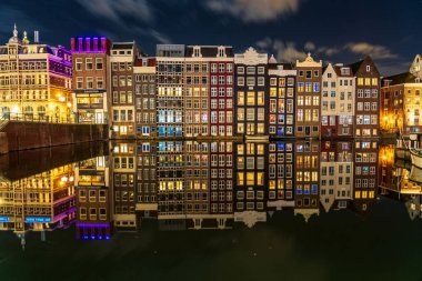 Damrak 'ın ikonik dans evleri, güzel aydınlatılmış ve sakin kanal sularına yansıyan, Amsterdam, Hollanda' nın kalbinde gece büyülü bir sahne yaratıyor.