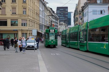 Basel, İsviçre. 22 Mart 2025: Basel eski kasabasında işlek bir cadde boyunca yeşil bir şehir tramvayı çalışıyor. Yüksek kalite fotoğraf