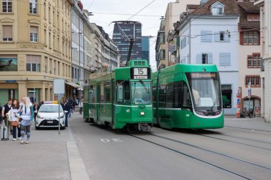 Basel, İsviçre. 22 Mart 2025: Basel eski kasabasında işlek bir cadde boyunca yeşil bir şehir tramvayı çalışıyor. Yüksek kalite fotoğraf