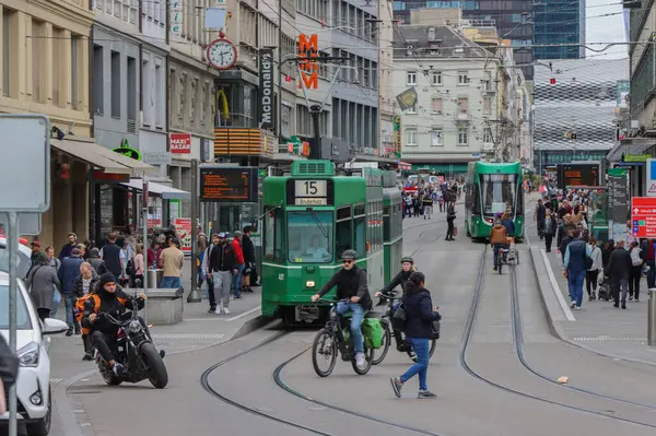 Basel, İsviçre. 22 Mart 2025: Basel eski kasabasında işlek bir cadde boyunca yeşil bir şehir tramvayı çalışıyor. Yüksek kalite fotoğraf