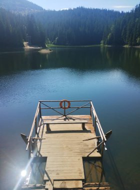 Sıcak bir gölü çevreleyen muhteşem dağ manzarası. Küçük liman bu fotoğrafın en önemli yeri. Hafif yaz serinliği cezbeder ve el değmemiş güzelliğiyle çağırır..