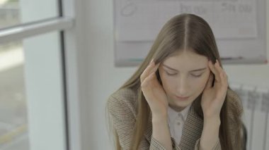 Genç bir kadın yoğun bir ofis ortamında masasında otururken gözle görülür bir stres belirtileri gösteriyor.
