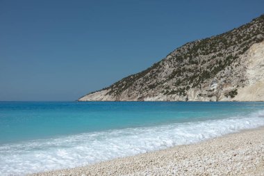 Turkuaz Akdeniz dalgaları kireçtaşı kayalıklarıyla beyaz çakıl taşı plajlarına yavaşça vuruyor.