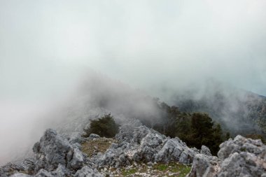Dağ zirveleri ve kireçtaşı oluşumları kalın bulutlarda gizlenmiş mistik atmosfer yaratıyor.