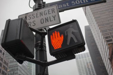 New York Şehri yaya geçidi işareti. Arka planda sokak işaretleri ve yüksek binalar olan turuncu el sembolü var.