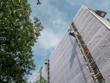 Yapı iskelesi ve koruyucu örtüsüyle bulutlu gökyüzüne karşı uçan kuşla kaplı.