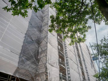 Yapım aşamasında olan çok katlı bina beyaz koruyucu iskele örtüsü ve iskeletle kaplı.