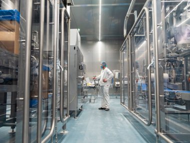 Beyaz üniformalı gıda işleme teknisyeni steril imalat tesisinde endüstriyel ekipman çalıştırıyor.