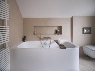 Beyaz banyo küveti, ahşap banyo seti, bej duvarlar ve modern ısıtmalı havlu radyatörü olan çağdaş banyo.