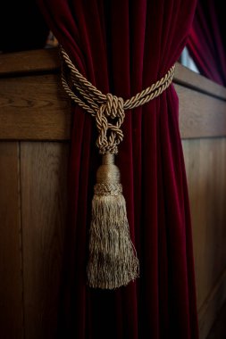 Şatafatlı iç mekan detaylarını gösteren bordo kadife perdelere karşı süslü altın püslü perdeler.