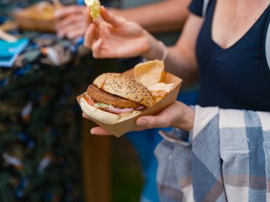 Açık hava kampı festivalinde elinde taze hamburger ve cips tutan biri.