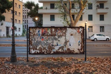 Sonbahar yapraklarıyla çevrili posterleri ve kağıtları olan eski ilan panosu.