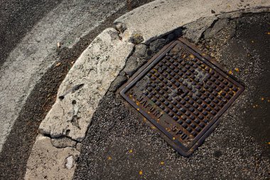 Sokak altyapısı rögar kapağını ve yıpranmış beton kaldırımı gösteriyor.