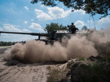 PZH2000NL topçuları mavi gökyüzünün altındaki kumlu arazide büyük toz bulutu yaratıyor