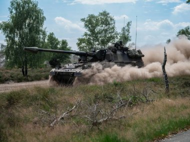 PZH2000NL ağır toz bulutu ve doğal bitki örtüsüyle arazide hareket ediyor.