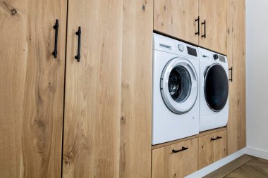Ahşap dolaptaki çamaşır makinesi ve kurutma makinesinin yan görüntüsü. Çağdaş çamaşır odası tasarımlı.