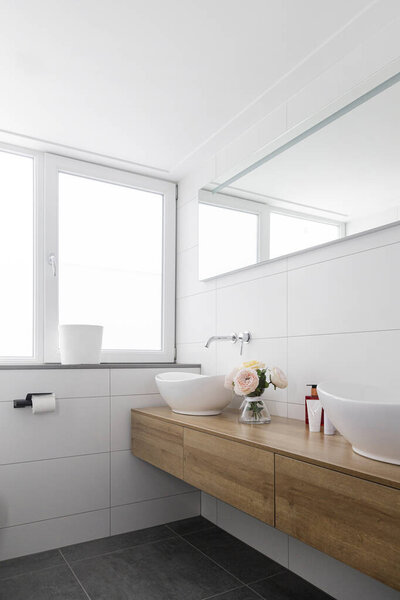 Современная ванная комната с плавающим деревянным тщеславием, раковинами, большими зеркалами и белыми стенами плитки