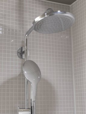 Modern duş başlığı ve elde taşınan krom eklentisi gri mozaik duvara sürtünüyor.