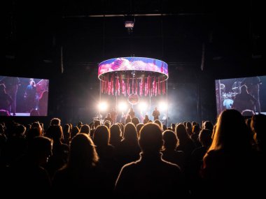 Kalabalık siluetleri ve atmosferik ışıklandırması olan büyük dairesel LED ekran kurulumunu içeren canlı performans