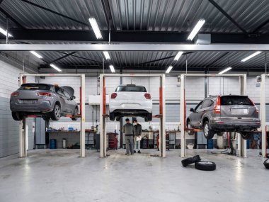 Modern ekipman ve aydınlatma ile profesyonel otomotiv onarım tesisinde hidrolik asansörlerle yükseltilmiş birden fazla araç