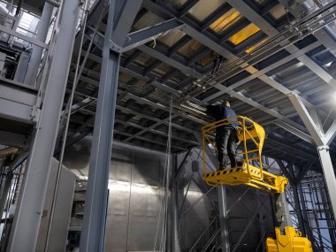 Sarı makas kaldırma büyük endüstriyel üretim tesisinde bakım için yüksek erişim sağlar
