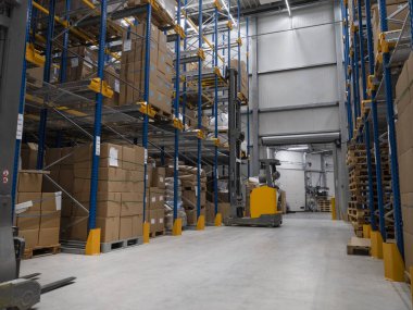 Depo koridorunda forklift ekipmanları ve ticari dağıtım tesisinde organize depolama sistemleri var.