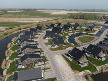 Modern konut geliştirme havadan bakıldığında, su kenarı konumu ve yeşil alanlar ile kıvrımlı sokak tasarımı gösteriliyor