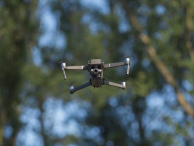 Quadcopter drone açık hava uçuş operasyonu sırasında bulanık orman arka planına karşı havada süzülüyor