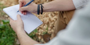 Doğal çevre koşullarında, organik arkaplan elementleriyle kağıt deftere yazılan eller.