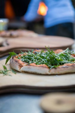 Tahta servis tahtasının üzerinde taze roka kaplı ahşap kaplı pizza.