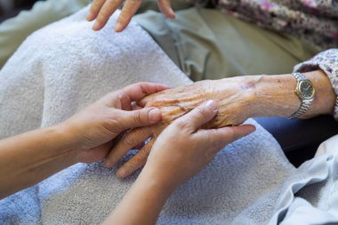 Nesiller boyu insan ilişkilerini gösteren saati olan yaşlı bir insanı destekleyen şefkatli eller.