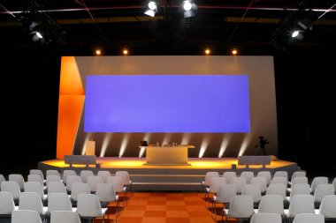 Turuncu ve mor markalaşma grafikleri, podyum kurulumu ve organize oturma düzeniyle profesyonel etkinlik sahnesi