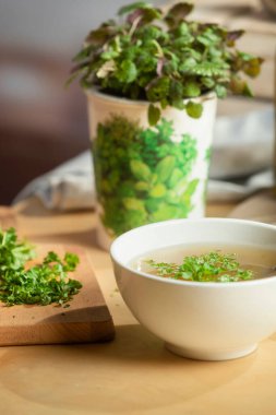 Mutfak sahnesinde sebzeli çorba, saksı bitkisi ve doğal ışıklandırmada eritilmiş yağ şişesi var.