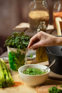 El baharatlı çorba, taze otlar, kereviz sapları ve tezgahta görünen yemek malzemeleri.