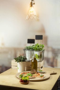 Pizza sahnesi, kolye ışıklandırması, taze bitkiler, yağ şişesi ve organize mutfak çalışma alanı.