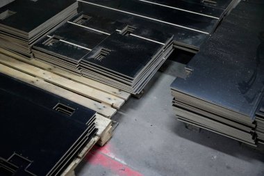 Endüstriyel üretim ortamında paletlerin üzerine yığılmış siyah malzeme panellerinin sistematik düzenlenmesi