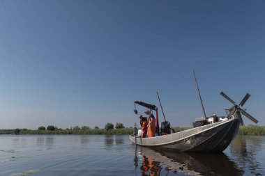 Turuncu güvenlik donanımlı bilim adamları geleneksel yel değirmeni yakınlarındaki Hollanda su yolu üzerinde çevre araştırması yürütüyorlar.