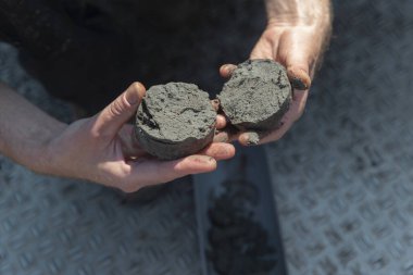 İç tortu yapısı ve bileşimini gösteren kırık toprak çekirdek örneklerinin iki yarısını tutan eller.