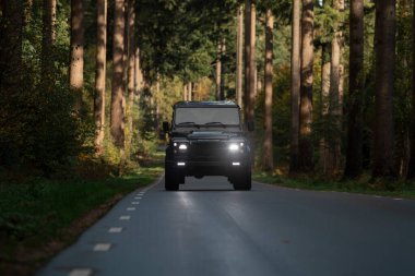 Forest Road 'daki 4x4 siyah aracın ön görüntüsü. Farları ve LED ışıkları aktif.