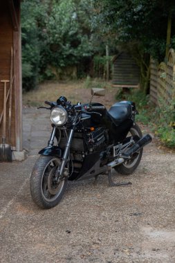 Kırsal kesimde ahşap bina olan çakıl yola park edilmiş siyah spor motosiklet.