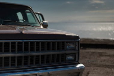 Aracın ön ızgarasında okyanus ve arka planda bulanık kıyı şeridi olan yakın çekim detayları.