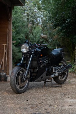 Çakıl taşı yüzeyinde, tahta yapıları ve doğal arka planı olan siyah spor motosikleti.