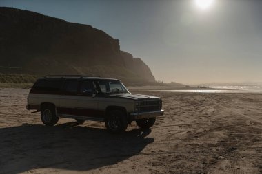 Kumlu sahildeki klasik SUV vagonu dramatik uçurumlar ve altın gün batımı ışıklandırmasıyla