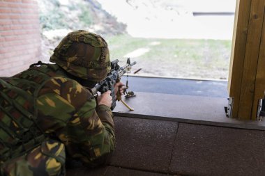 Kamuflaj üniformalı askeri personel, kapalı alanda atış poligonu kurmayı hedefliyor.