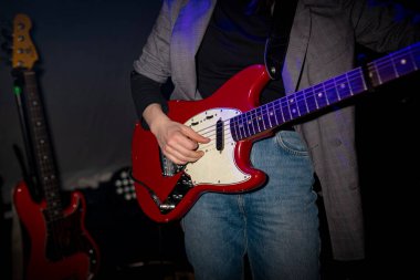 Konser ortamında mavi ışıklandırmalı kırmızı elektro gitar çalan müzisyen.