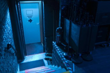 Mavi ışıklı ve soyunma odası tabelasıyla dramatik bir sahne arkası merdiveni.