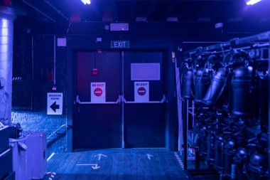 Sahne arkasında mavi ışıklandırma ve yön işareti olan bir tiyatro.